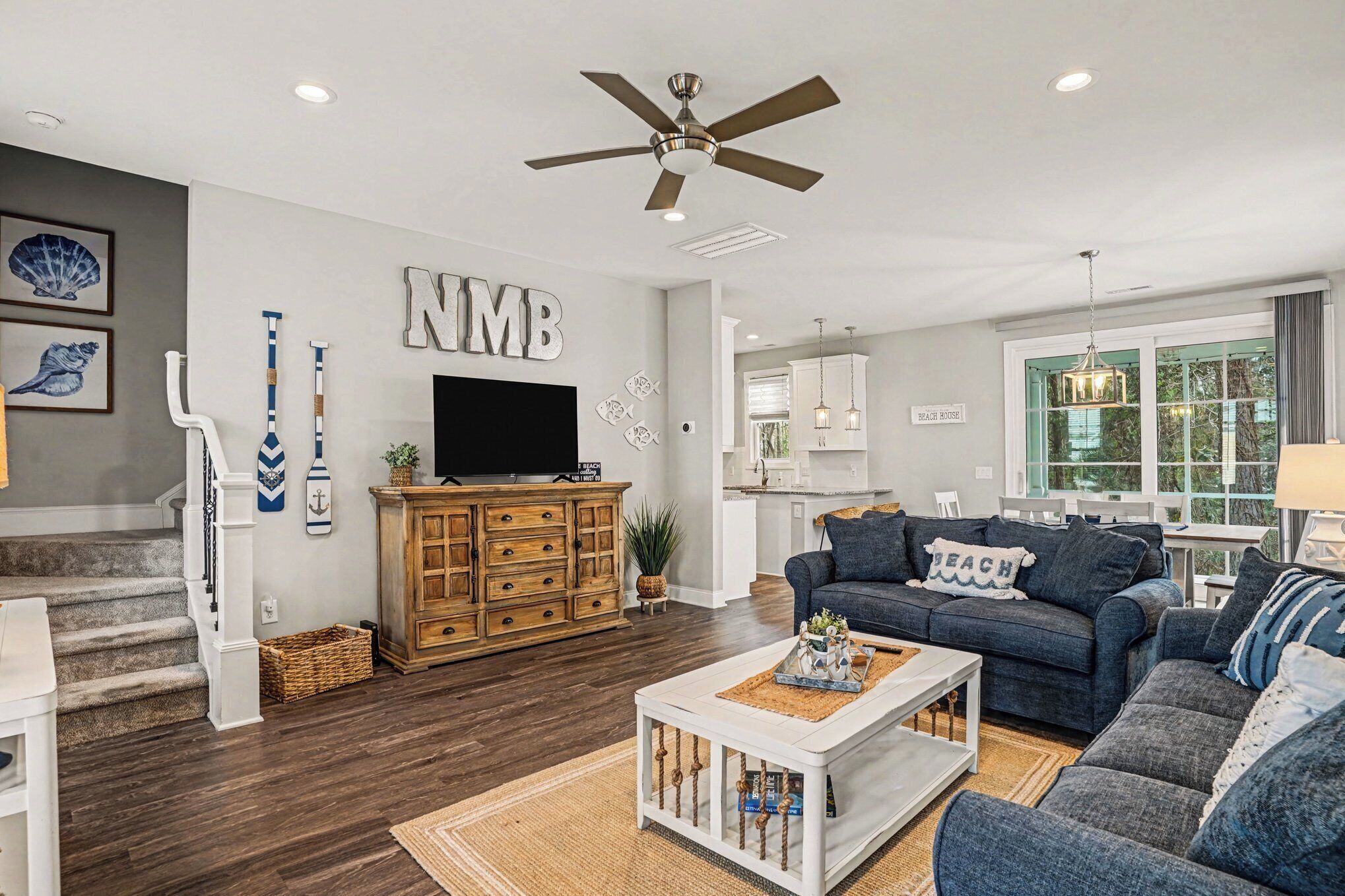 A modern living room with a dark wood floor, a white coffee table, a blue sofa, and a ceiling fan.