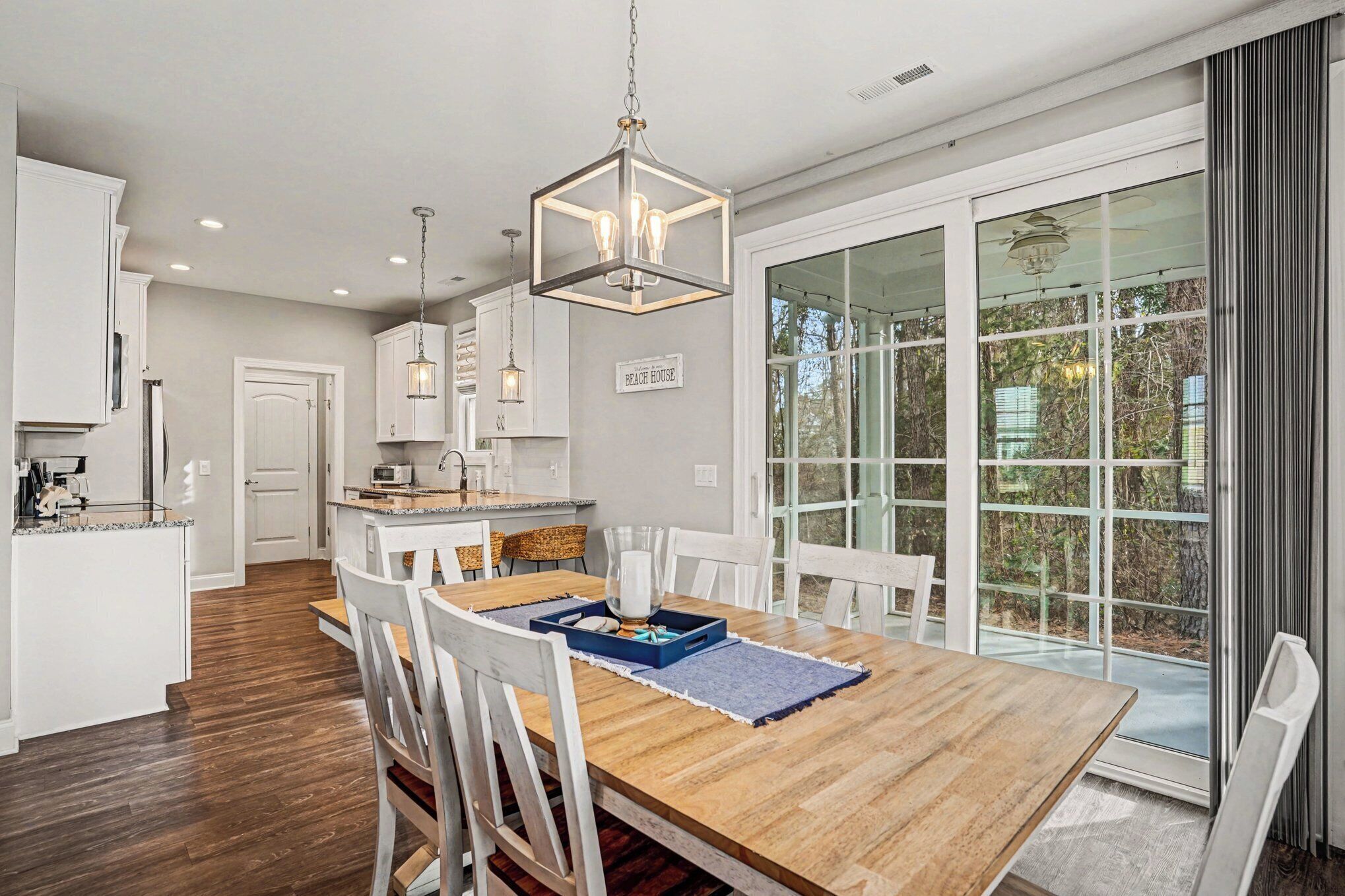 A spacious kitchen with a wooden dining table, white chairs, and a large window with a view of trees.