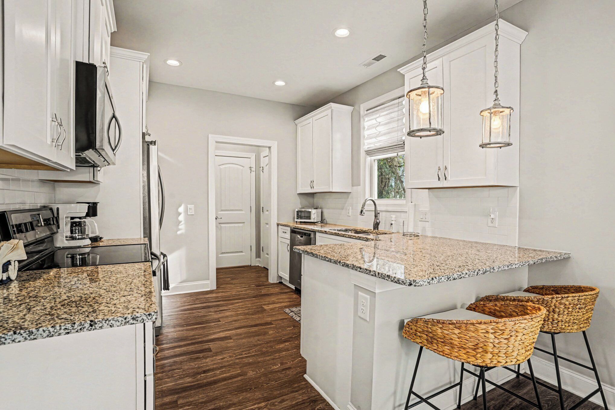 A kitchen with white cabinets, granite countertops, and a central island with bar stools.