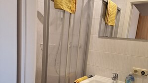 Un baño con cabina de ducha de vidrio, un lavabo con mueble de madera y un espejo sobre el lavabo.