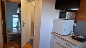 Una cocina compacta equipada con microondas, refrigerador y un pequeño mostrador con tostadora y una botella de detergente.