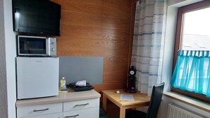 Una kitchenette compacta con microondas, refrigerador y una pequeña mesa con silla.