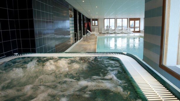 Een wellnessruimte met een jacuzzi, betegelde muren en een zwembad.