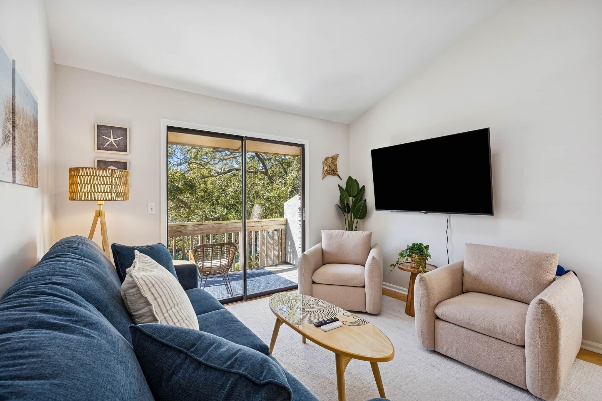Een woonkamer met een bank, fauteuils, een salontafel, een televisie en een balkon met uitzicht op bomen.