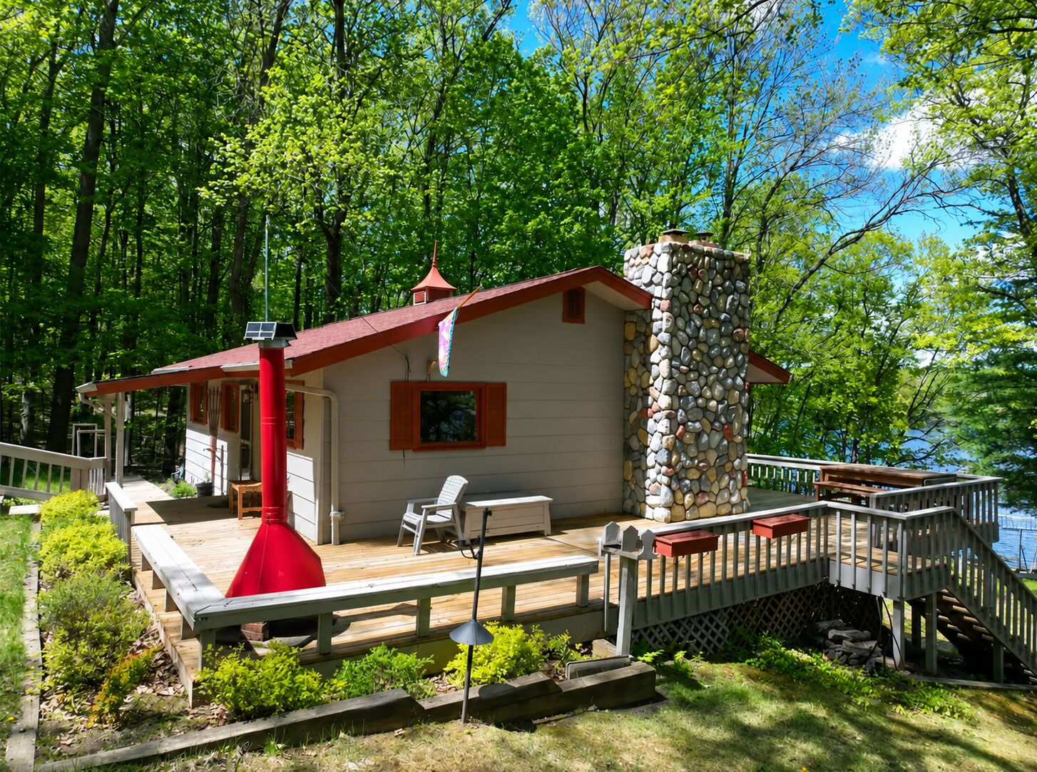 A cabin with a stone chimney, a deck, and a small porch.