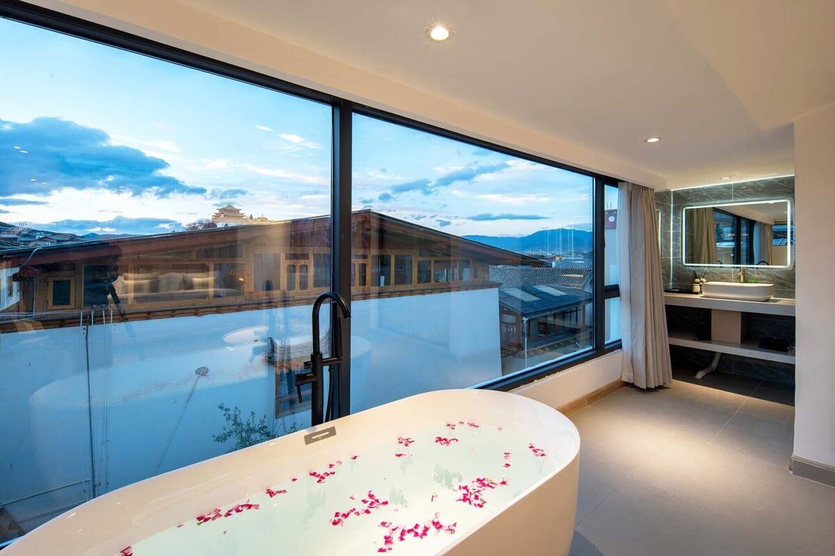 A modern bathroom with a large bathtub, a glass shower enclosure, and a view of a traditional building through large windows.
