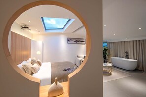 Une chambre moderne avec une lucarne, un grand lit, une table de chevet et une vue sur une salle de bain avec une baignoire et des rideaux.