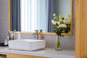 Une salle de bain avec un lavabo blanc, un miroir et un vase contenant des fleurs blanches.