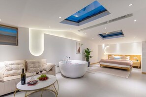 A modern bedroom with a skylight, a large bathtub, a sofa, and a bedside table with a bottle and grapes. - Shangri-La Jingyue Homestay (Deqin)