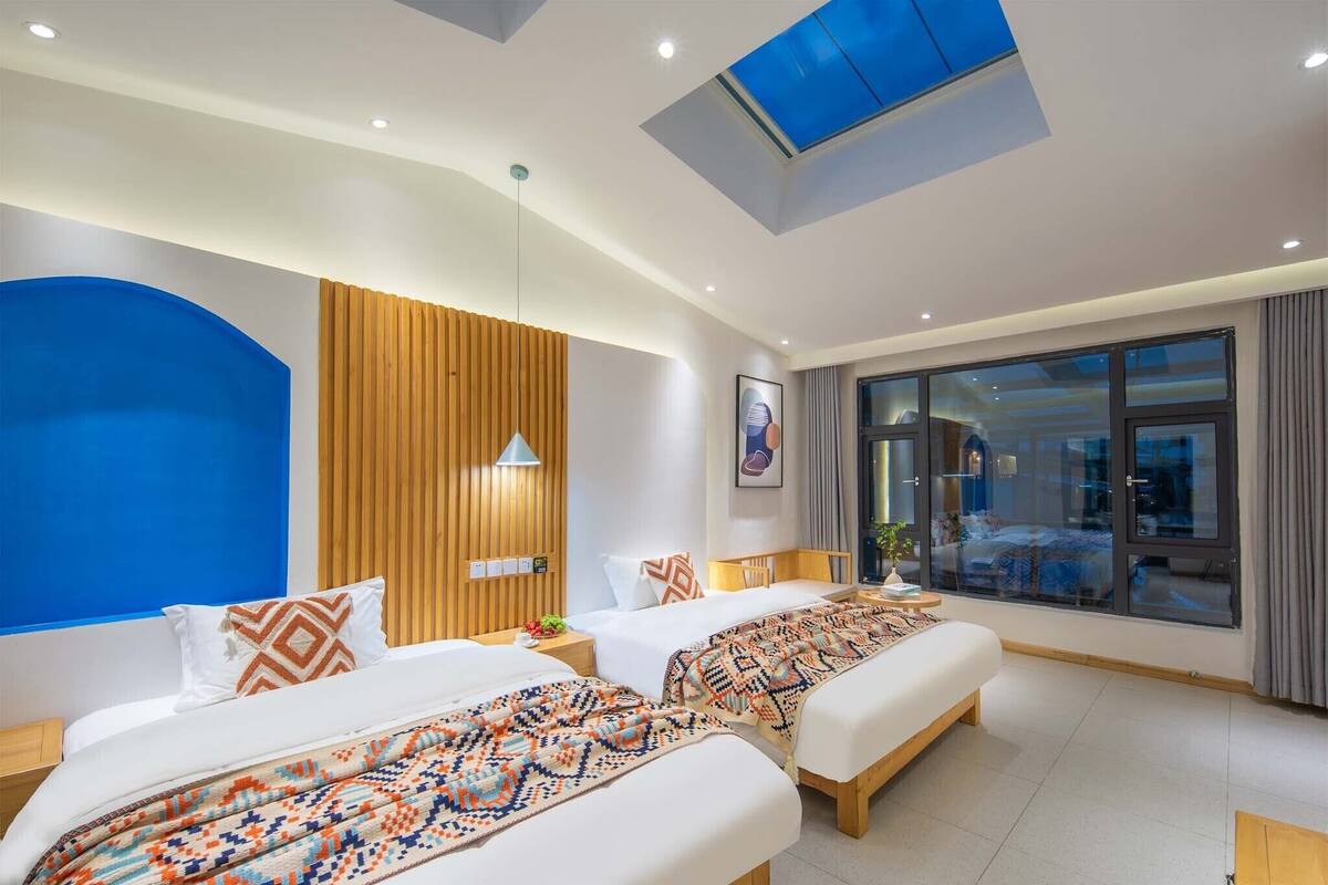 A modern hotel room with two beds, a skylight, a large window, and a view of the city.