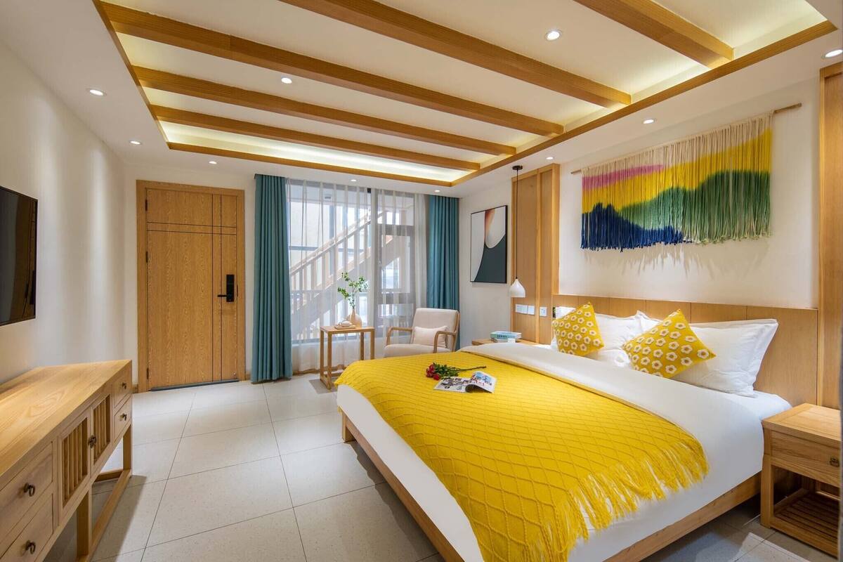 A modern hotel room with a large bed, wooden ceiling beams, a TV, a desk, and a staircase.