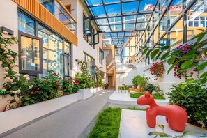 A modern hotel corridor with glass ceilings, indoor plants, and a red sculpture. - Shangri-La Jingyue Homestay (Deqin)