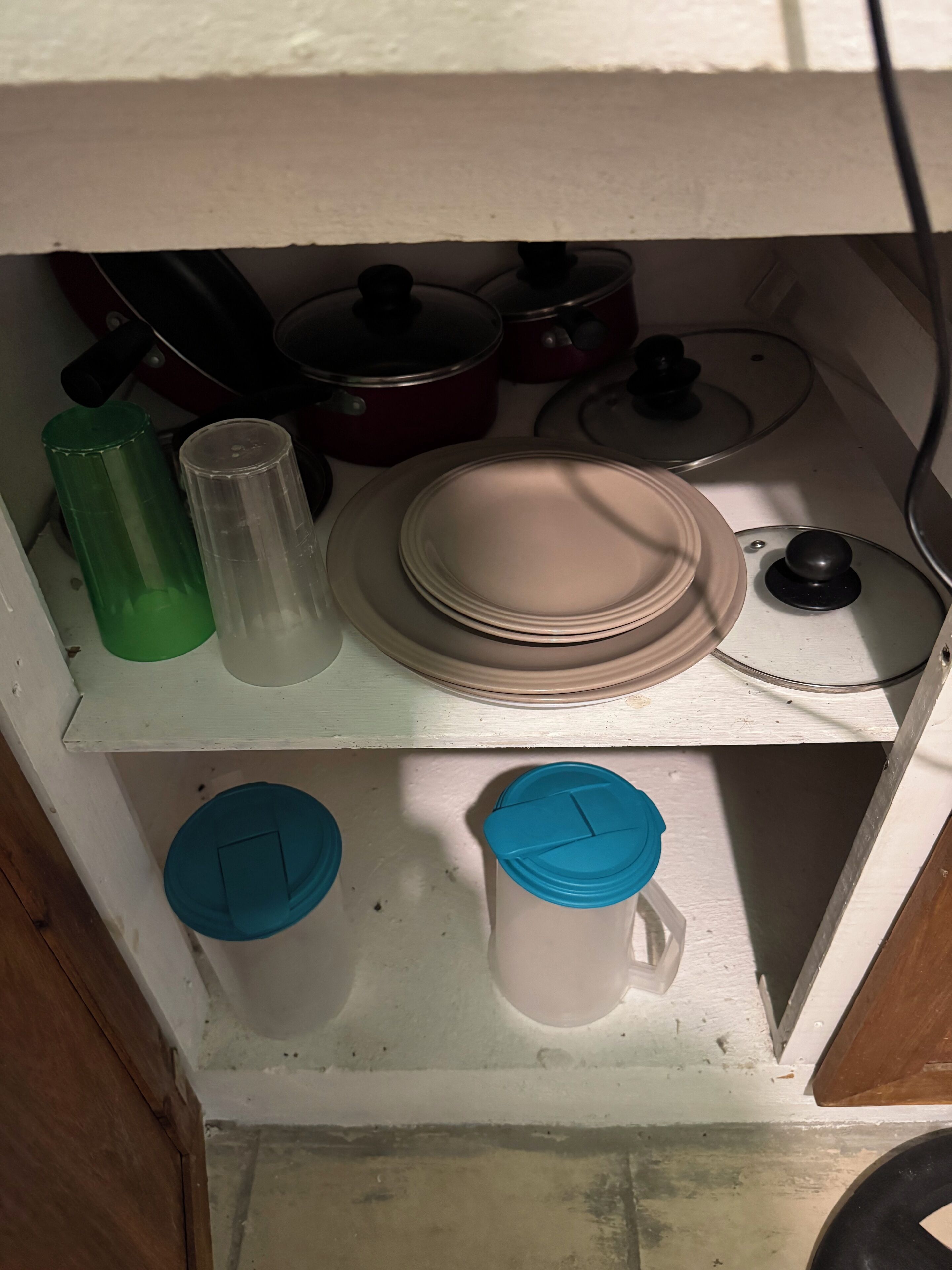 Una cocina con encimera blanca, una botella de agua verde, un vaso transparente, una pila de platos blancos, una olla roja y una jarra de agua azul.