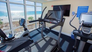 Ein Fitnessraum mit Laufbändern und Fernseher, mit Blick auf einen Strand.