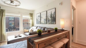 Quarto de hotel moderno com cama, sofá, escrivaninha com luminária e vista para um edifício.