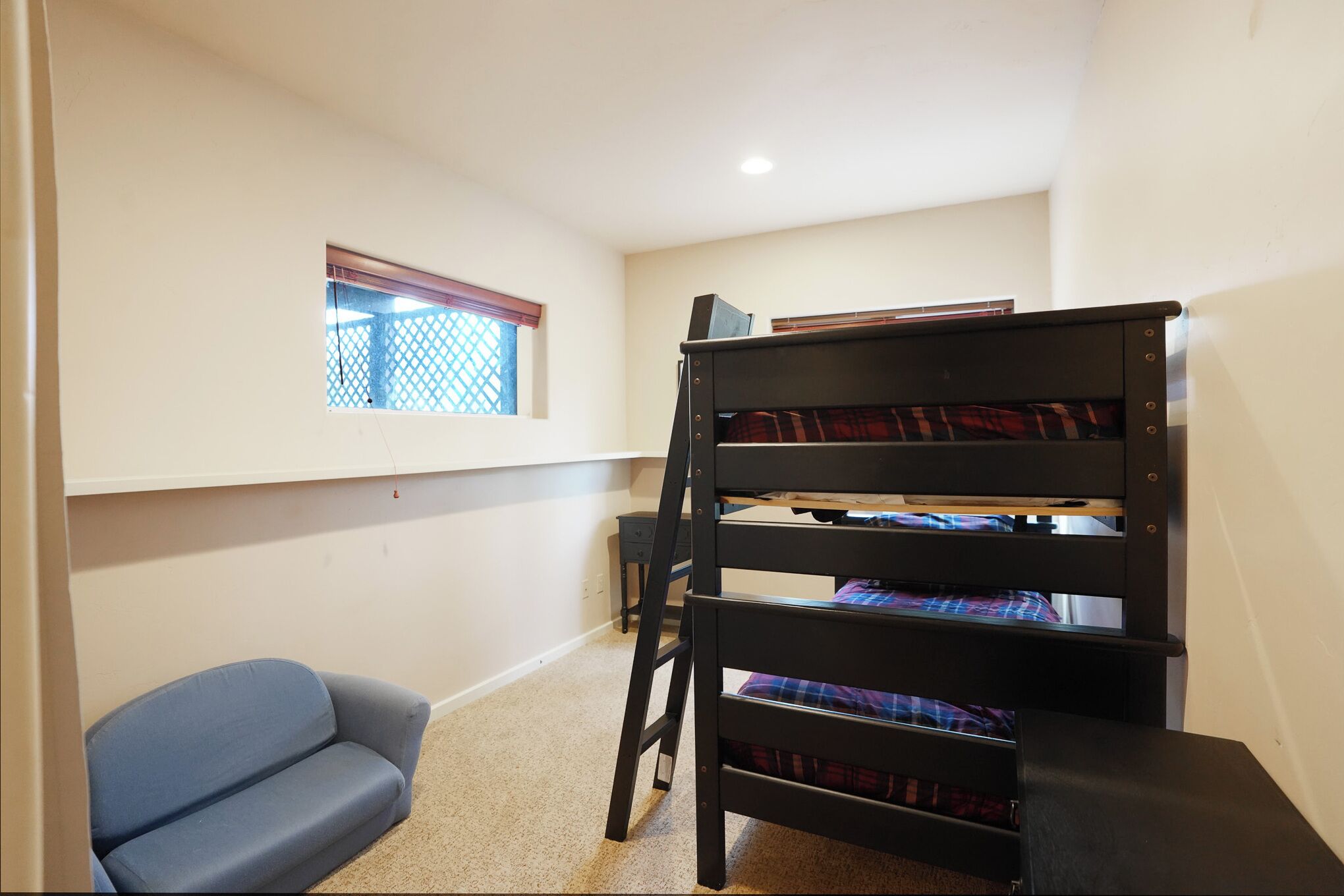A bunk bed with a ladder, a small sofa, and a window with blinds.