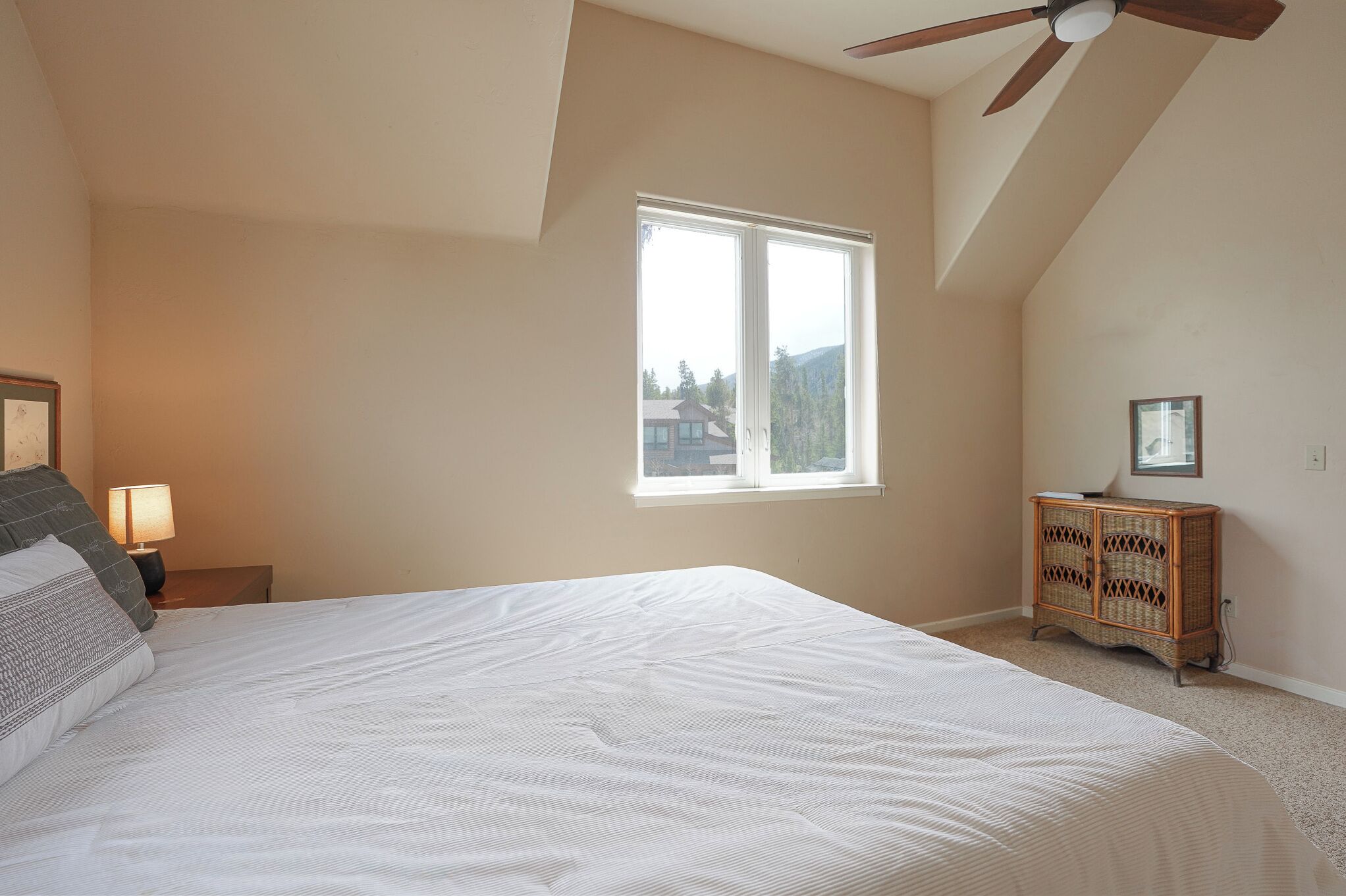 Un dormitorio con cama, ventana, ventilador de techo, mesita de noche y armario.