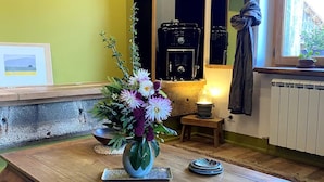 Une pièce chaleureuse avec une table basse en bois, un vase de fleurs, un tableau encadré et une fenêtre avec des rideaux.
