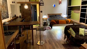 Un espace de vie compact comprenant un coin cuisine, un coin repas, un lit et un espace détente avec un canapé et un fauteuil.