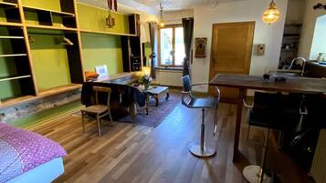 Una sala de estar acogedora con piso de madera, un comedor con mesa y sillas, una cocina con pileta, y un ventanal que deja entrar luz natural.