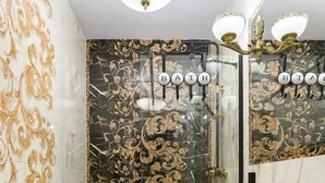 A bathroom with a black and gold patterned wall, a white sink with gold fixtures, and a chandelier. - Malila Apartments Cracow Lubicz 14 (Kraków)