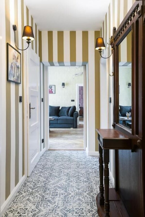 A hallway with striped walls, patterned flooring, and a dark wooden console table with a mirror. - Malila Apartments Cracow Lubicz 14 (Kraków)