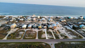 An aerial view of a coastal residential area with houses on stilts, a road in the foreground, and the ocean in the background. - Doodle Dunes: New! Private Pool + Dog Friendly (Gulf Shores)