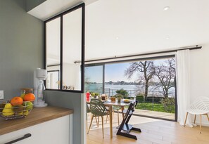 A modern kitchen with a large window overlooking a scenic view. - -FLORA- Family home on Penfoulic cove (La Forêt-Fouesnant)