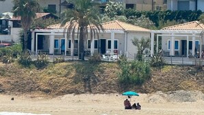Hotel a la costa amb múltiples balcons, una platja al primer pla i vista al mar.