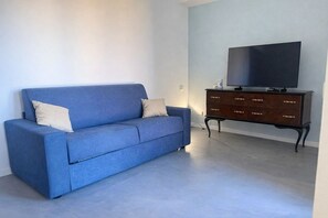 Un salon avec un canapé bleu, une commode en bois foncé et un téléviseur à écran plat.