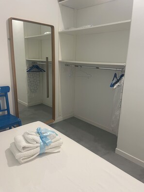 A hotel room with a bed, a blue chair, a wardrobe with hangers, and a mirror. - Galleria 28. Holiday in style – By the sea (Soverato)