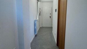 Passadís estret i ben il·luminat amb una porta de fusta al final, parets blanques i una catifes gris.