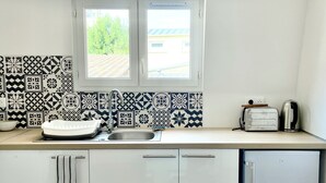 Een moderne keuken met witte kastjes, een spoelbak, een raam en een broodrooster op het aanrecht.