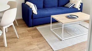 Een moderne woonkamer met een blauwe bank, witte stoelen, een houten salontafel en een witte vloer.