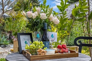 Ein Gartentisch mit einem bordgestellten Willkommensschild, einer Weinflasche, einem Glas, Trauben, Erdbeeren und einer Schale mit Nüssen.