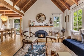 A cozy living room with a fireplace, wooden furniture, and a view of the outdoors. - 4069 Twin Briar Cottage -Fairytale Carmel Home (Carmel-by-the-Sea)