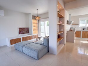 A modern kitchen with built-in wooden cabinets, a dining area with a grey sofa, and a pendant light. - Villa Rhodéa | Private Heated Pool | 180sqm | 200m to Sea | 10 people (Ialisos)