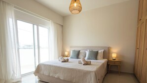 Hotellihuone, jossa on suuri sänky, yöpöytä lampun kanssa, ikkuna verhoilla ja pyöreä matto.
