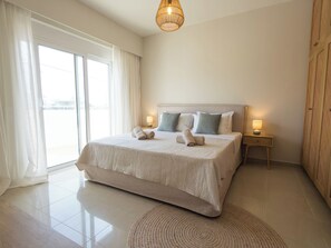 A hotel room with a large bed, a bedside table with a lamp, a window with curtains, and a circular rug. - Villa Rhodéa | Private Heated Pool | 180sqm | 200m to Sea | 10 people (Ialisos)