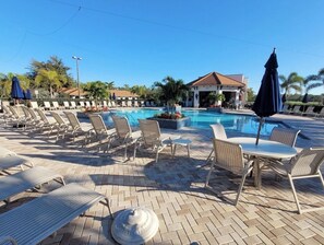 Un espace aménagé au bord de la piscine, avec des chaises longues et des parasols, un petit pavillon et une piscine à l’eau d’un bleu limpide.