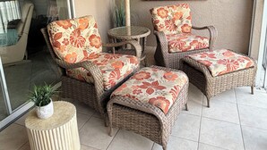 Un patio soleado con muebles de mimbre, una puerta de cristal que da al exterior, un cuadro en la pared y un ventilador de techo.