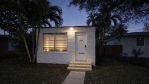 Una casa moderna de un piso con fachada blanca, puerta principal y un pequeño jardín delantero con un sendero que lleva a la entrada.