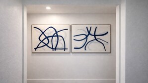 Dos cuadros abstractos en una pared lisa en un pasillo con suelo de madera.