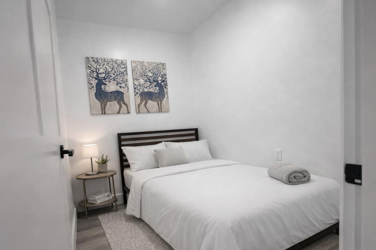 Un dormitorio con cama, mesita de noche, lámpara y dos cuadros en la pared.