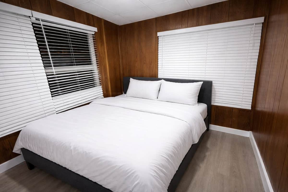 Un dormitorio con cama, paredes de madera y persianas blancas.