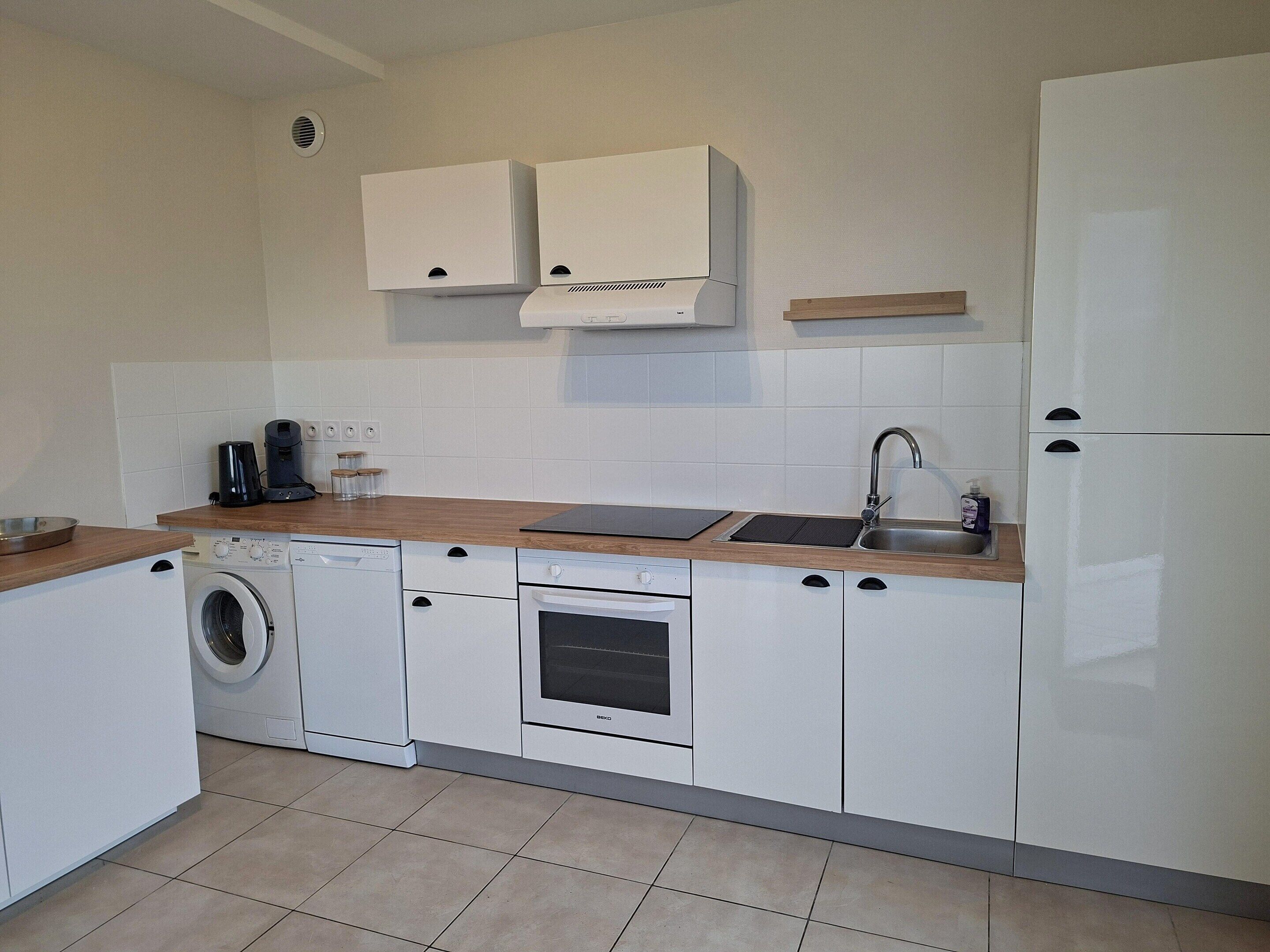 A compact kitchen with a washing machine, oven, and a sink with a faucet.
