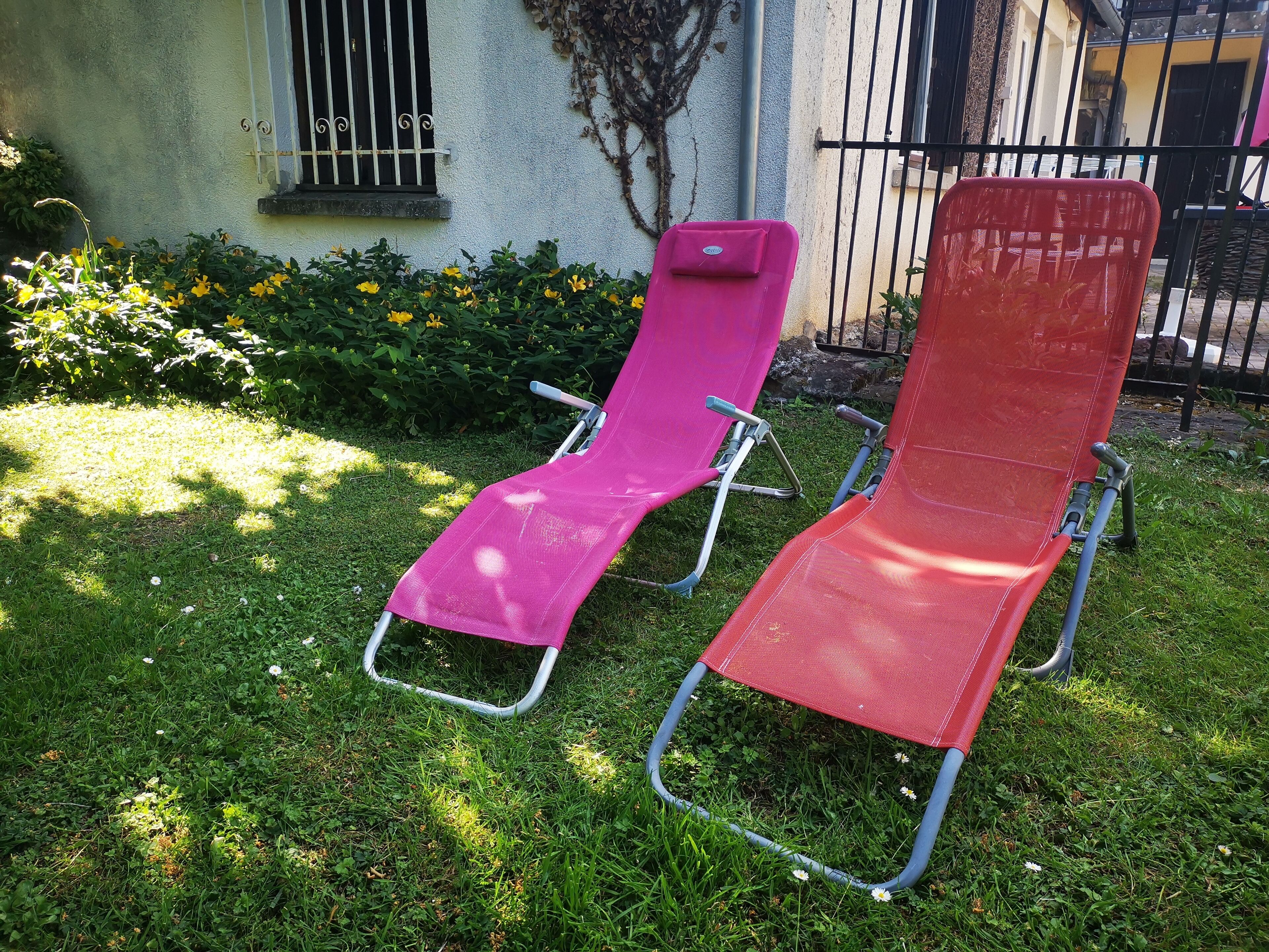 Two outdoor lounge chairs in a grassy area with a building in the background.