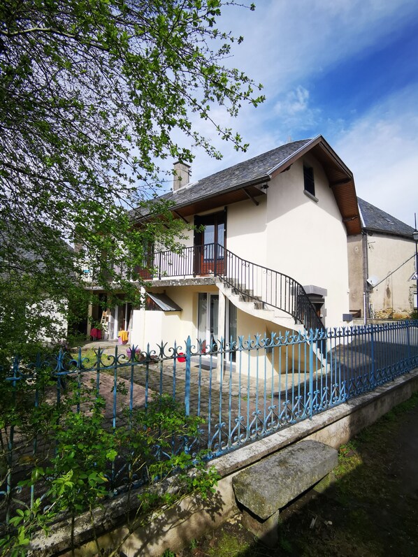 A two-story house with a balcony, a stone pathway, and a blue metal fence.