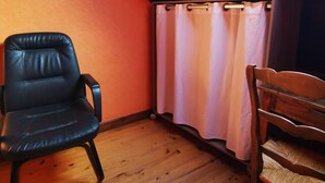 A room with wooden flooring, a black leather chair, a wooden chair, and a window with a curtain. - Calme et détente assurée (Avèze)