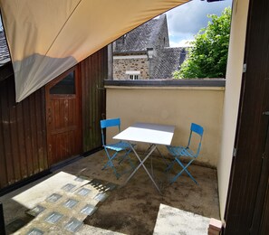 A small outdoor patio with a table and two chairs, a wooden door, and a stone wall.